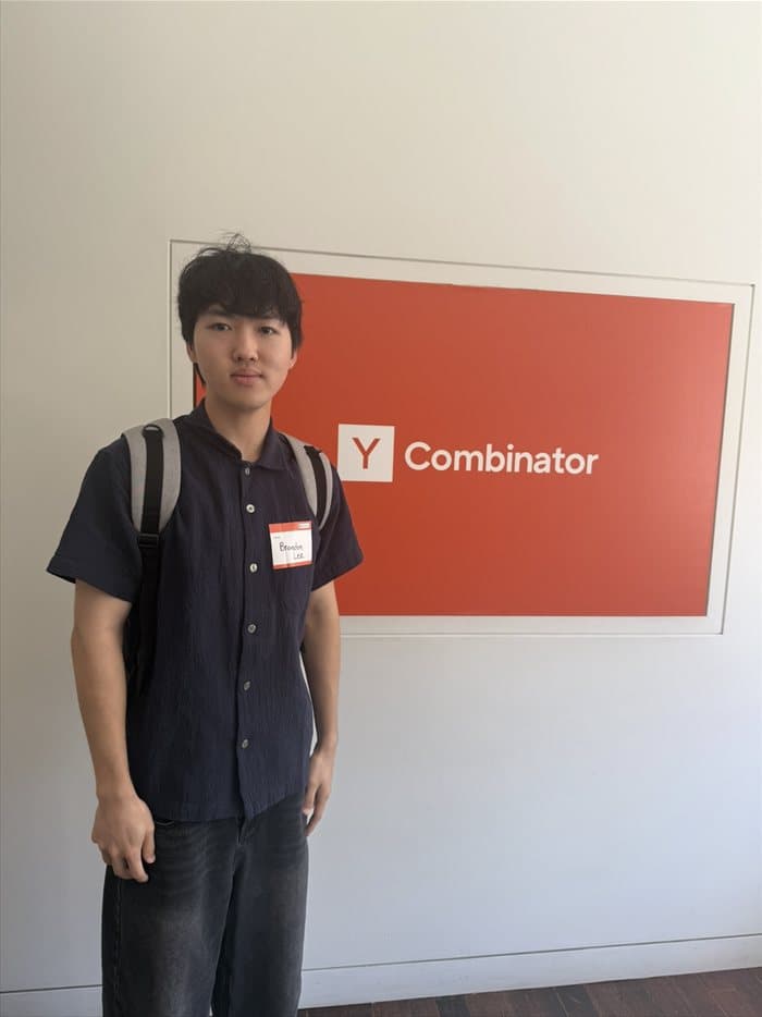 Brandon standing in front of the Y Combinator sign wearing a name tag
